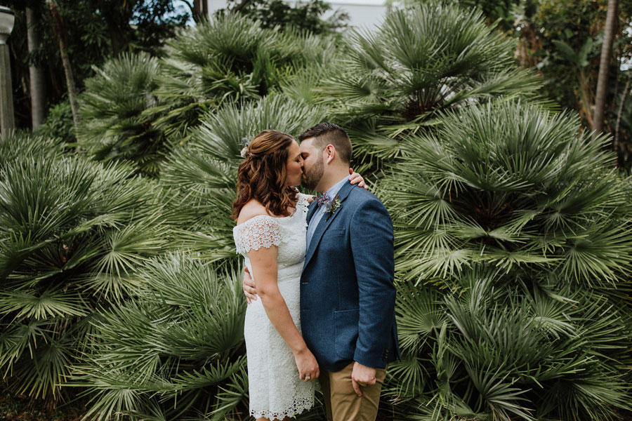 Bride and Groom kiss in front of foliage in park