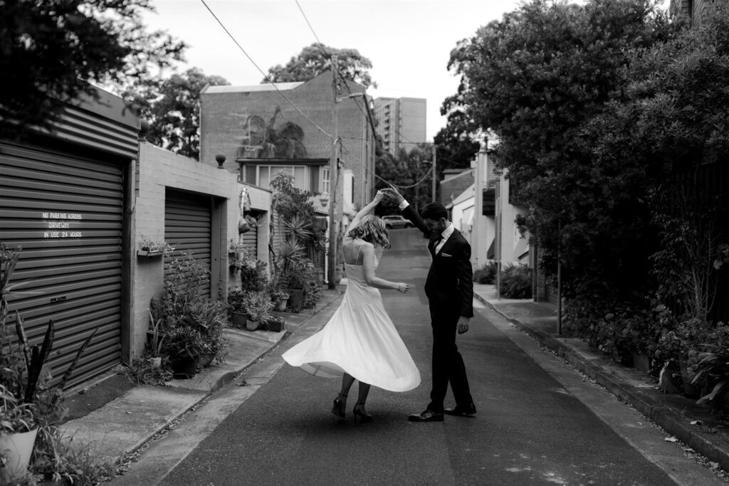 Groom twirling bride in quiet street.