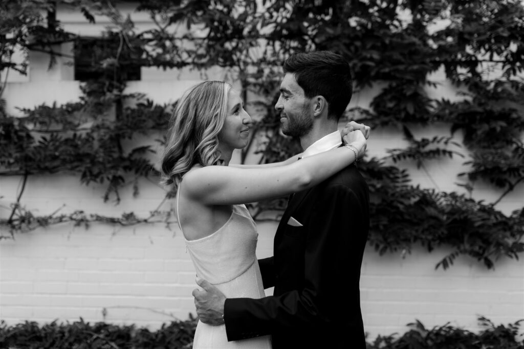 Bride and groom embracing in front of leafy wall in black and white