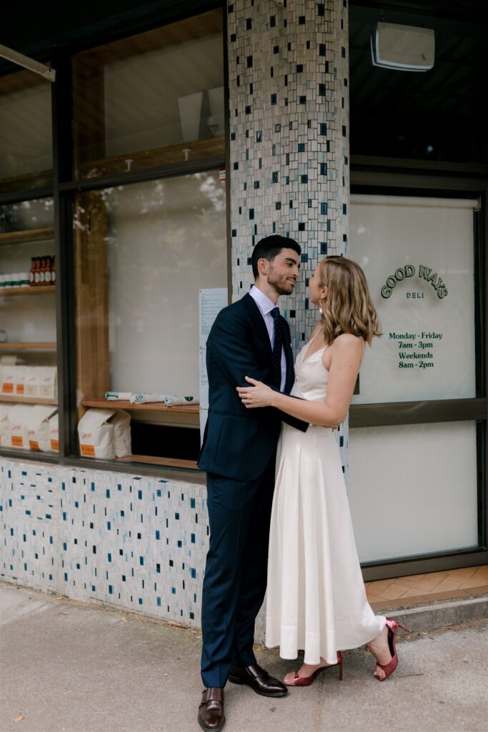 Bride and groom embracing on street corner outside store