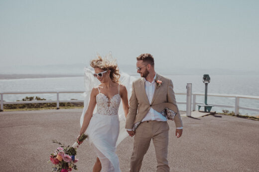 Bride and groom at Byron Bay lighthouse on windy day with sea in background